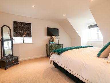 A bedroom with a bed a dresser with a mirror a wall mounted tv and a standing mirror at Trevose House in Crantock