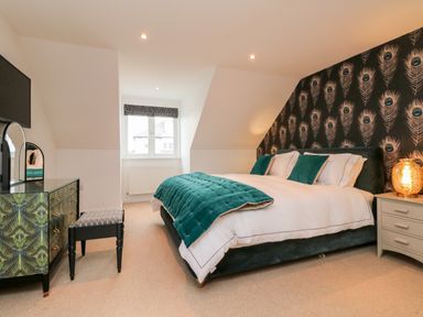 A bedroom with a bed a dresser with mirror and a window at Trevose House in Crantock