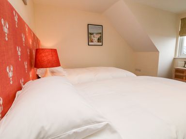 A bedroom with two beds white bedding red headboard with lobster pattern a red lamp a framed picture and a window at Trevose House in Crantock