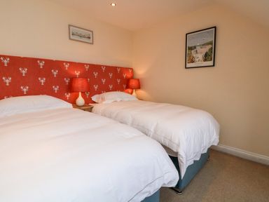 A bedroom with two single beds with white bedding and red lamps on a bedside table at Trevose House in Crantock
