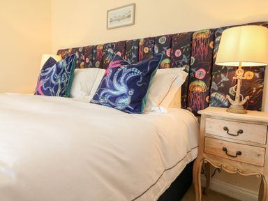 A bed with patterned headboard and pillows next to a wooden nightstand with a lamp at Trevose House in Crantock