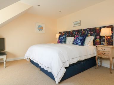 A bedroom with a large bed two pillows two bedside tables with lamps and a television on a small table at Trevose House in Crantock