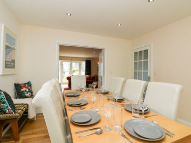 A dining room with a table set for eight and a bench with cushions at Trevose House in Crantock