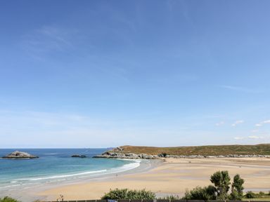 A sandy beach with a few people and rocky headlands with the ocean and blue sky at Trevose House in Crantock