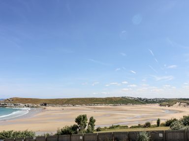 A sandy beach with people near the water and hills in the background at Trevose House in Crantock