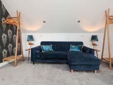 A room with a blue sofa and peacock patterned cushions with two wooden clothes racks and two side tables with lamps at Trevose House in Crantock