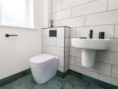 A bathroom with a toilet and a wall-mounted sink with a black faucet at Trevose House in Crantock