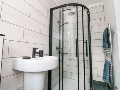 A bathroom with a corner shower enclosure with black frame a white pedestal sink and a towel rack with blue towels at Trevose House in Crantock