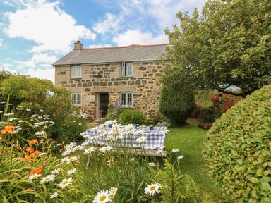 A stone cottage with a slate roof surrounded by a garden with flowers and a picnic table at Higher Roskorwell Cottage in St Keverne