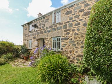 Stone cottage with shrubs and flowers in the garden at Higher Roskorwell Cottage in St Keverne