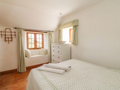 A bedroom with a bed folded towels a white chest of drawers and windows with green check curtains at Higher Roskorwell Cottage in St Keverne