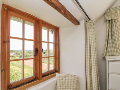 A window with wooden frame curtains and a cushion in a room at Higher Roskorwell Cottage in St Keverne