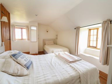 A bedroom with two single beds pillows blankets two windows with curtains a wooden door and a wall mirror at Higher Roskorwell Cottage in St Keverne