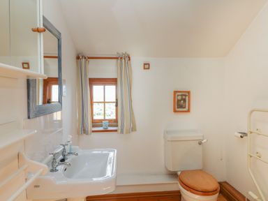 A bathroom with a sink mirror window toilet with wooden seat and wall art at Higher Roskorwell Cottage in St Keverne
