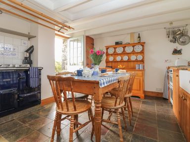 A kitchen with wooden chairs and table set for tea with blue checkered tablecloth and open door at Higher Roskorwell Cottage in St Keverne