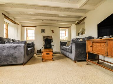 A living room with two gray sofas a wooden chest as a coffee table a stone fireplace and a wooden TV stand at Higher Roskorwell Cottage in St Keverne