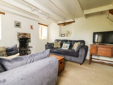 A living room with two gray sofas cushions a wooden chest an old stone fireplace a wooden TV stand and a television at Higher Roskorwell Cottage in St Keverne