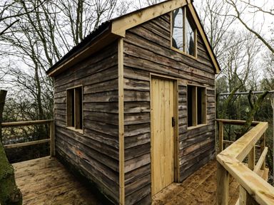 A small wooden cabin with a deck and railings surrounded by leafless trees at High Cogges Farm Holiday Cottages - The Cart Shed High Cogges near Witney