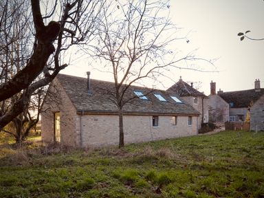 Stone buildings with sloped roofs and skylights surrounded by grass and leafless trees at High Cogges Farm Holiday Cottages near Witney