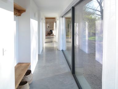 A hallway with a wooden bench and baskets and a glass wall with curtains at High Cogges Farm Holiday Cottages - The Cart Shed in High Cogges near Witney
