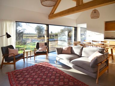 A living room with a gray sofa and two armchairs near large windows and a wooden dining table at High Cogges Farm Holiday Cottages - The Cart Shed High Cogges near Witney