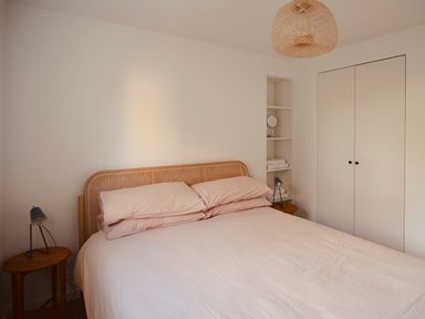 A bedroom with a bed and wooden headboard bedside tables with lamps shelves with towels and a mirror and a wardrobe at High Cogges Farm Holiday Cottages - The Cart Shed High Cogges near Witney