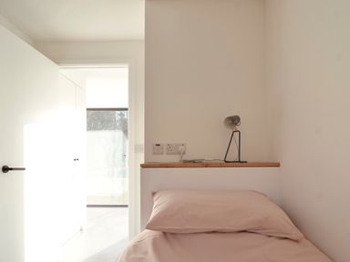 A bedroom with a single bed pink bedding and a small lamp on a shelf next to an open door at High Cogges Farm Holiday Cottages - The Cart Shed High Cogges near Witney