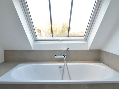A bathtub with a handheld showerhead under a skylight window at High Cogges Farm Holiday Cottages - The Cart Shed in High Cogges near Witney