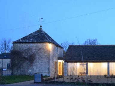 Stone building with a weather vane and a modern extension with large windows at High Cogges Farm Holiday Cottages - The Cart Shed High Cogges near Witney
