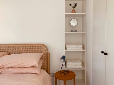 A bedroom with a wooden bed and pink bedding next to white shelves holding towels a mirror and a vase with flowers at High Cogges Farm Holiday Cottages - The Cart Shed High Cogges near Witney