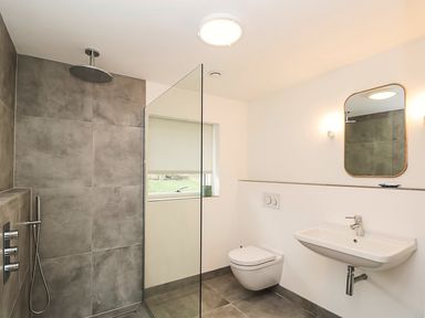 A bathroom with a walk-in shower, wall-mounted toilet, sink, and mirror at High Cogges Farm Holiday Cottages - The Cart Shed High Cogges near Witney