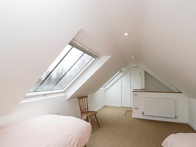 An attic bedroom with two beds a wooden chair a radiator and skylight windows at High Cogges Farm Holiday Cottages - The Cart Shed in High Cogges near Witney