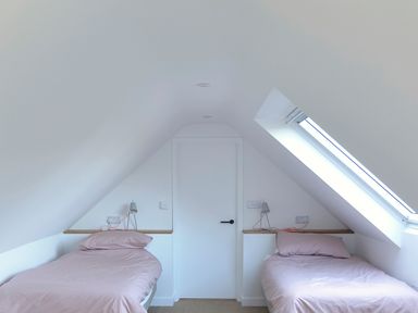A bedroom with two single beds under slanted ceilings and a skylight at High Cogges Farm Holiday Cottages - The Cart Shed in High Cogges near Witney