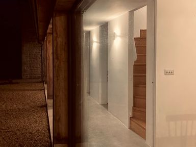 A hallway with wooden stairs and wall lights visible through a glass door at High Cogges Farm Holiday Cottages - The Cart Shed in High Cogges near Witney