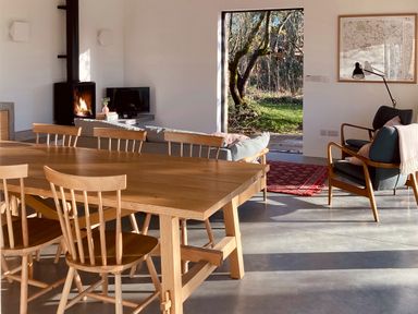 A dining area with wooden table and chairs next to a living space with sofa fireplace and armchairs at High Cogges Farm Holiday Cottages - The Cart Shed High Cogges near Witney