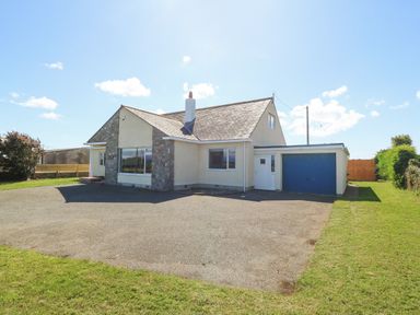 A detached house with a stone and cream exterior a driveway and a blue garage door at Glanffraw in Aberffraw Ty Croes