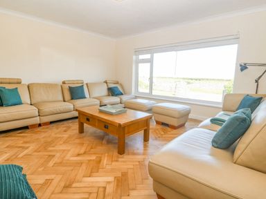 A living room with leather sofas and blue cushions around a wooden coffee table at Glanffraw in Aberffraw Ty Croes