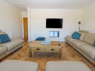 A living room with beige sofas blue cushions a wooden coffee table and a wall mounted TV at Glanffraw in Aberffraw Ty Croes