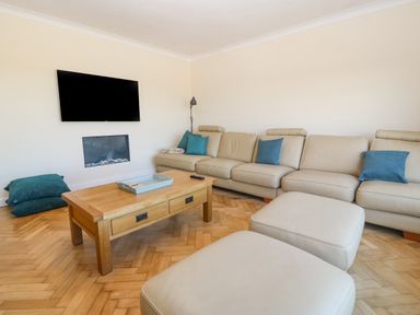 A living room with a beige sectional sofa and blue pillows a wooden coffee table a wall-mounted television and a fireplace at Glanffraw in Aberffraw Ty Croes