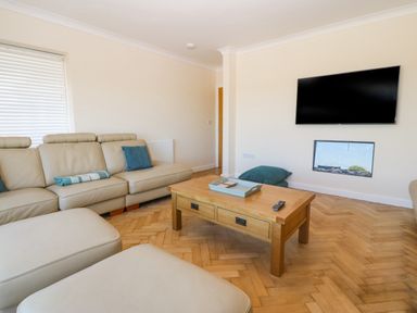 A living room with beige sofas a wooden coffee table a wall-mounted television and a small fireplace at Glanffraw in Aberffraw Ty Croes