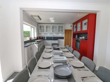 A kitchen with a long dining table set with plates and cutlery and grey chairs at Glanffraw in Aberffraw Ty Croes