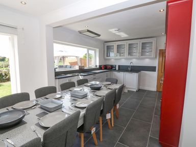 A kitchen with a long dining table set with plates and bowls and grey chairs at Glanffraw in Aberffraw Ty Croes