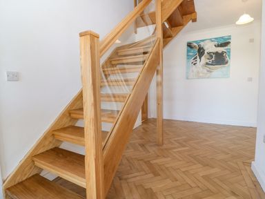 A wooden staircase with glass paneling in a hallway with a parquet floor and a painting of a cow on the wall at Glanffraw in Aberffraw Ty Croes