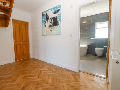 An interior hallway with wooden herringbone flooring a door to a bathroom and a painting of a cow in Glanffraw Aberffraw Ty Croes