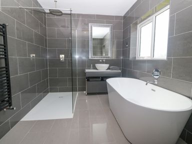 A bathroom with a freestanding bathtub a walk in shower a sink with a mirror above it and a window at Glanffraw in Aberffraw Ty Croes