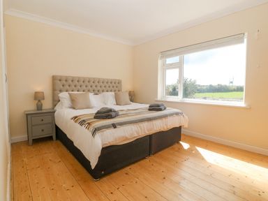 A bedroom with a bed pillows bedside tables lamps and a large window at Glanffraw Aberffraw Ty Croes
