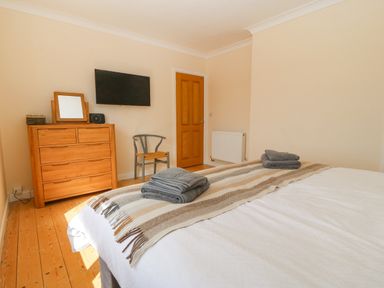 A bedroom with a wooden dresser chair mounted tv and a bed with folded towels at Glanffraw in Aberffraw Ty Croes