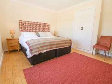 A bedroom with a bed a wooden floor two bedside tables with lamps a chair and a closet at Glanffraw in Aberffraw Ty Croes