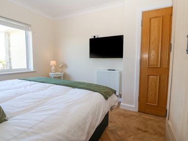 A bedroom with a bed a bedside table with a lamp a wall-mounted television and a wooden door at Glanffraw in Aberffraw Ty Croes