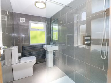 A bathroom with a toilet a sink a shower area with glass partition and tiled walls at Glanffraw in Aberffraw Ty Croes